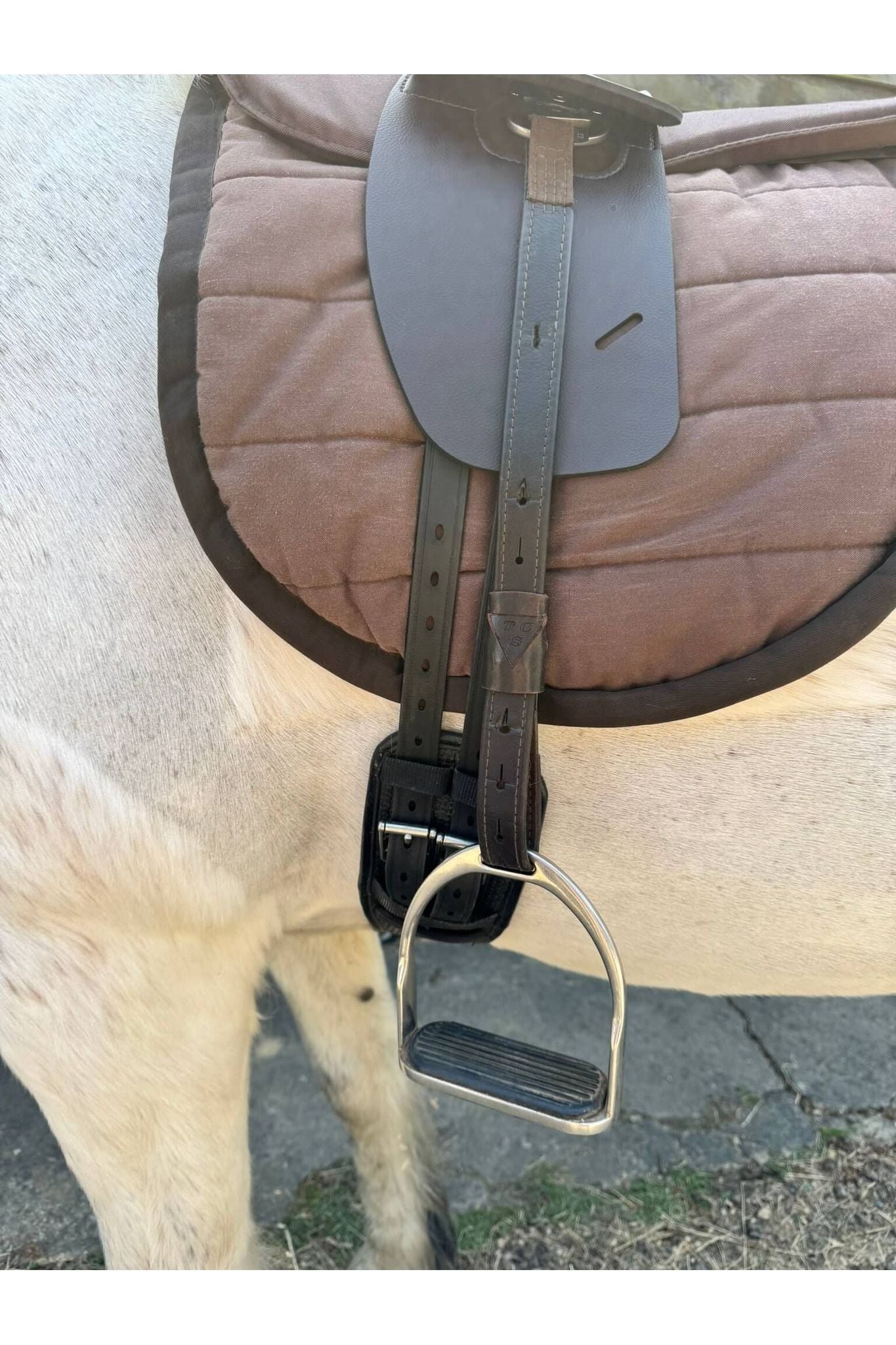A synthetic chocolate brown Total Contact Saddle close up on a brown saddle pad and a brown half pad on a grey pony
