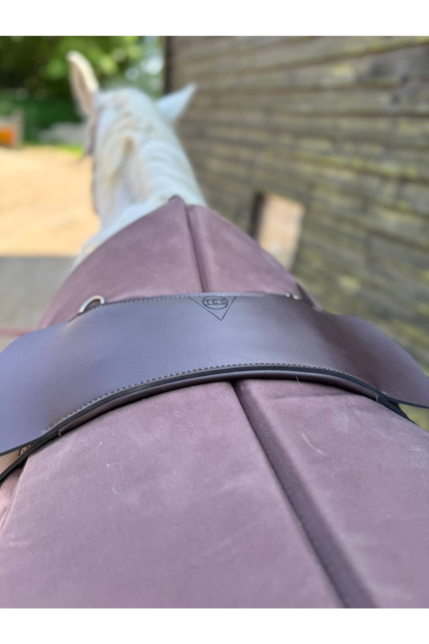 A synthetic chocolate brown treeless Total Contact Saddle close up on a brown saddle pad and a brown half pad on a grey pony