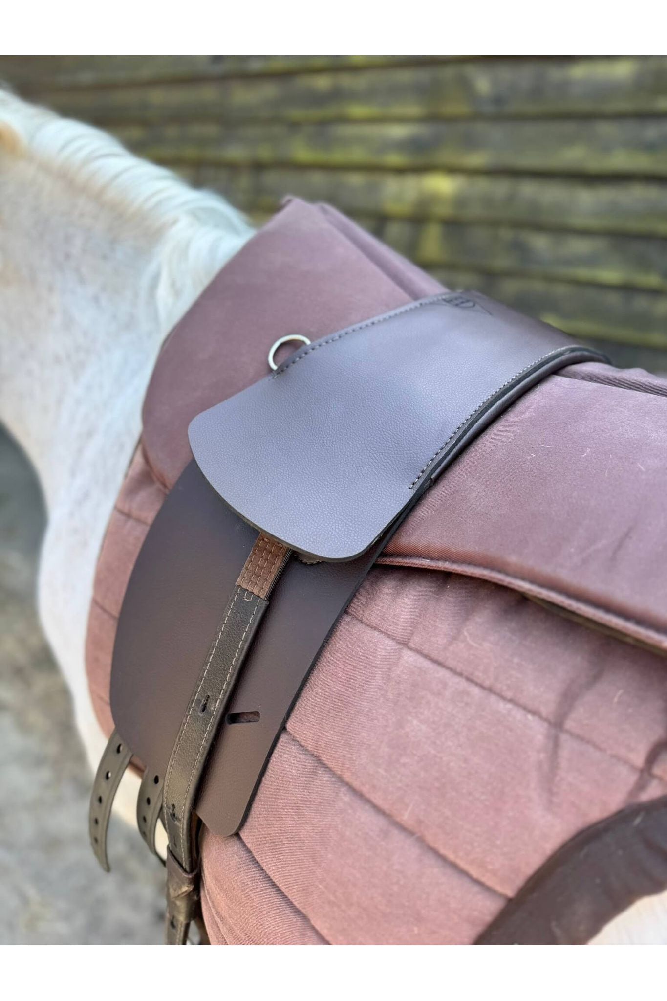 A synthetic chocolate brown treeless Total Contact Saddle on a brown saddle pad and a brown half pad on a grey pony