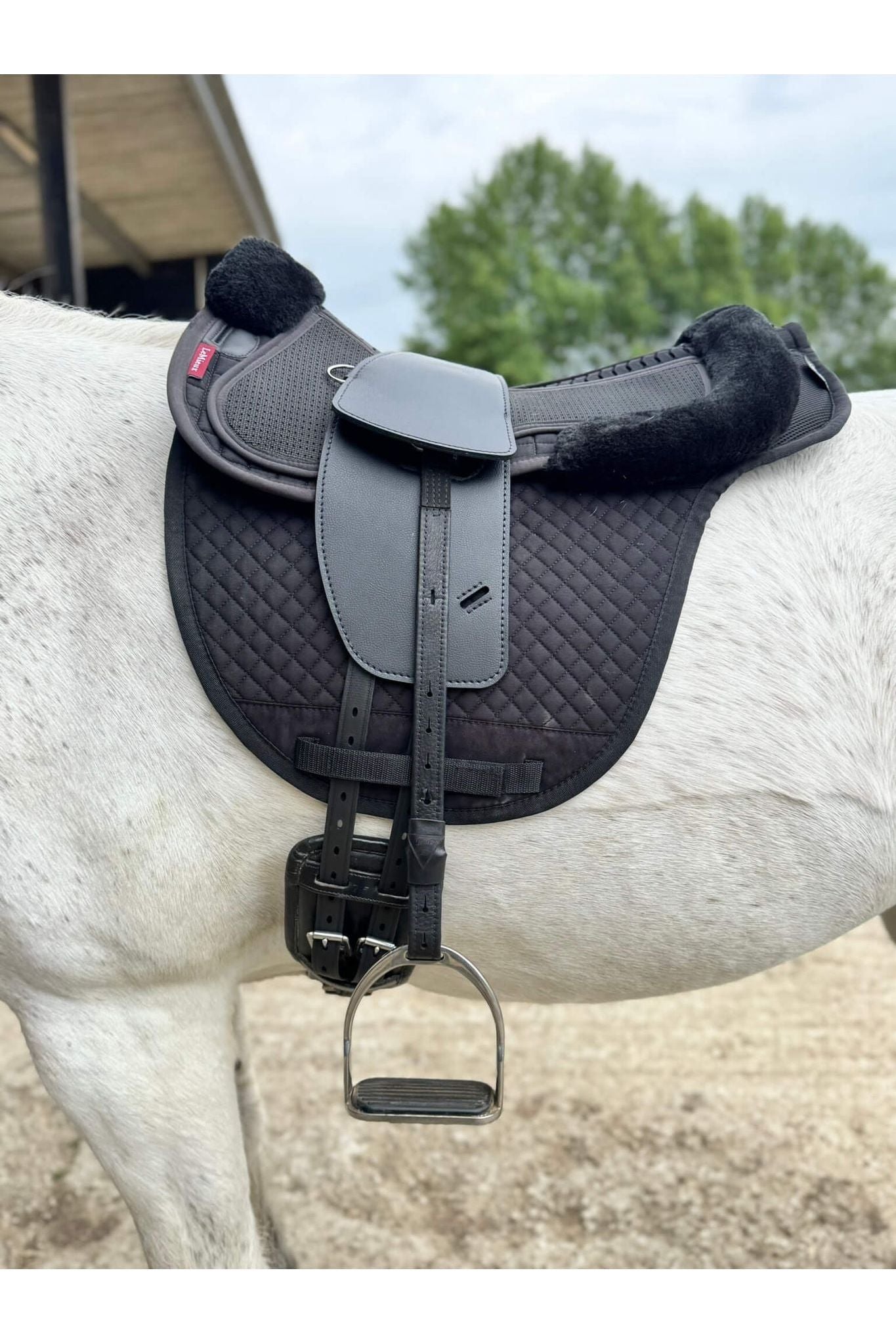 A synthetic black long billet Total Contact Saddle close up on a black saddle pad and a black half pad on a grey pony