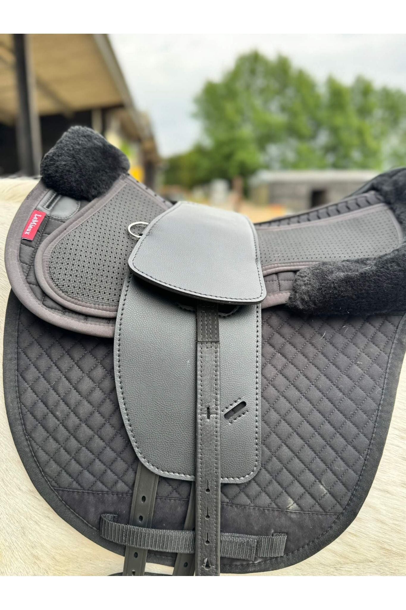 A synthetic black long billet Total Contact Saddle close up on a black saddle pad and a black half pad on a grey pony