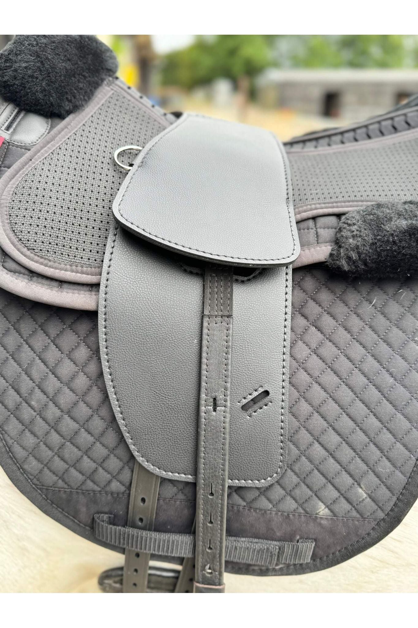 A synthetic black long billet Total Contact Saddle close up on a black saddle pad and a black half pad