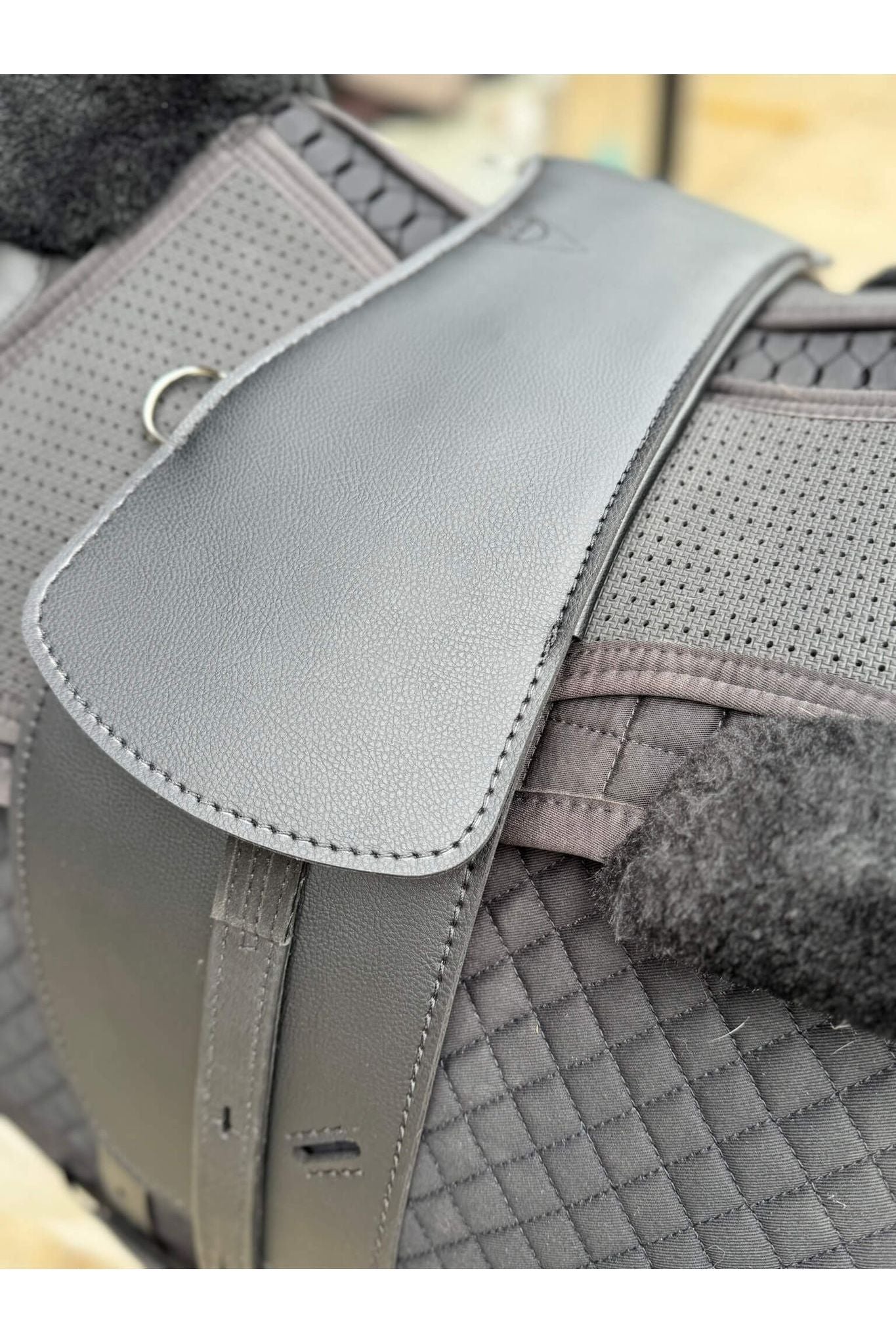 A synthetic black long billet Total Contact Saddle close up on a black saddle pad and a black half pad