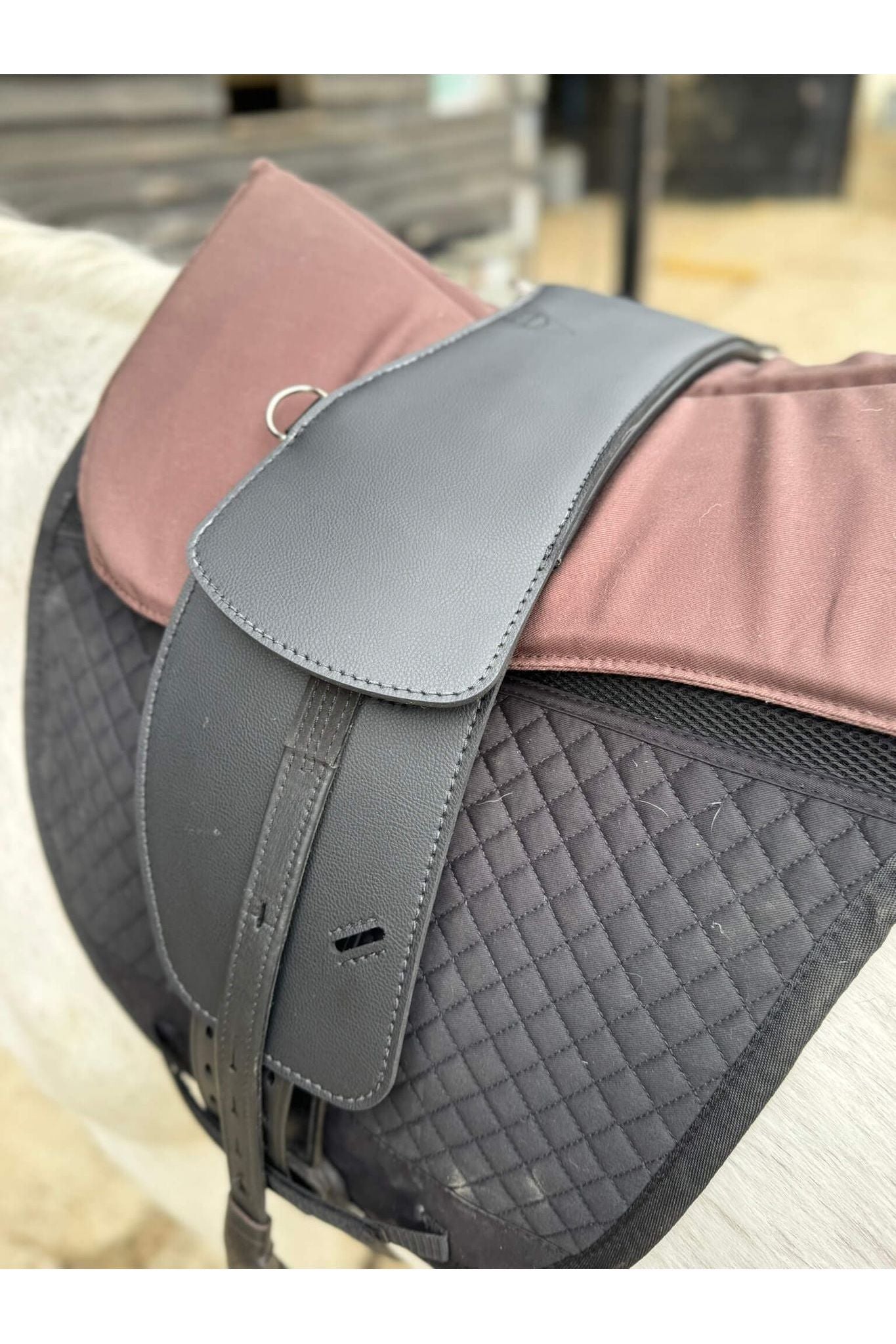 A synthetic black short billet Total Contact Saddle close up on a black saddle pad and a brown half pad on a grey pony