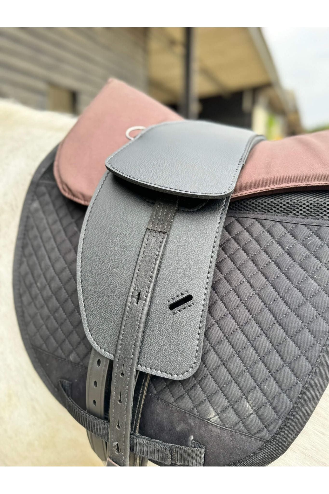 A synthetic black short billet Total Contact Saddle close up on a black saddle pad and a brown half pad on a grey pony