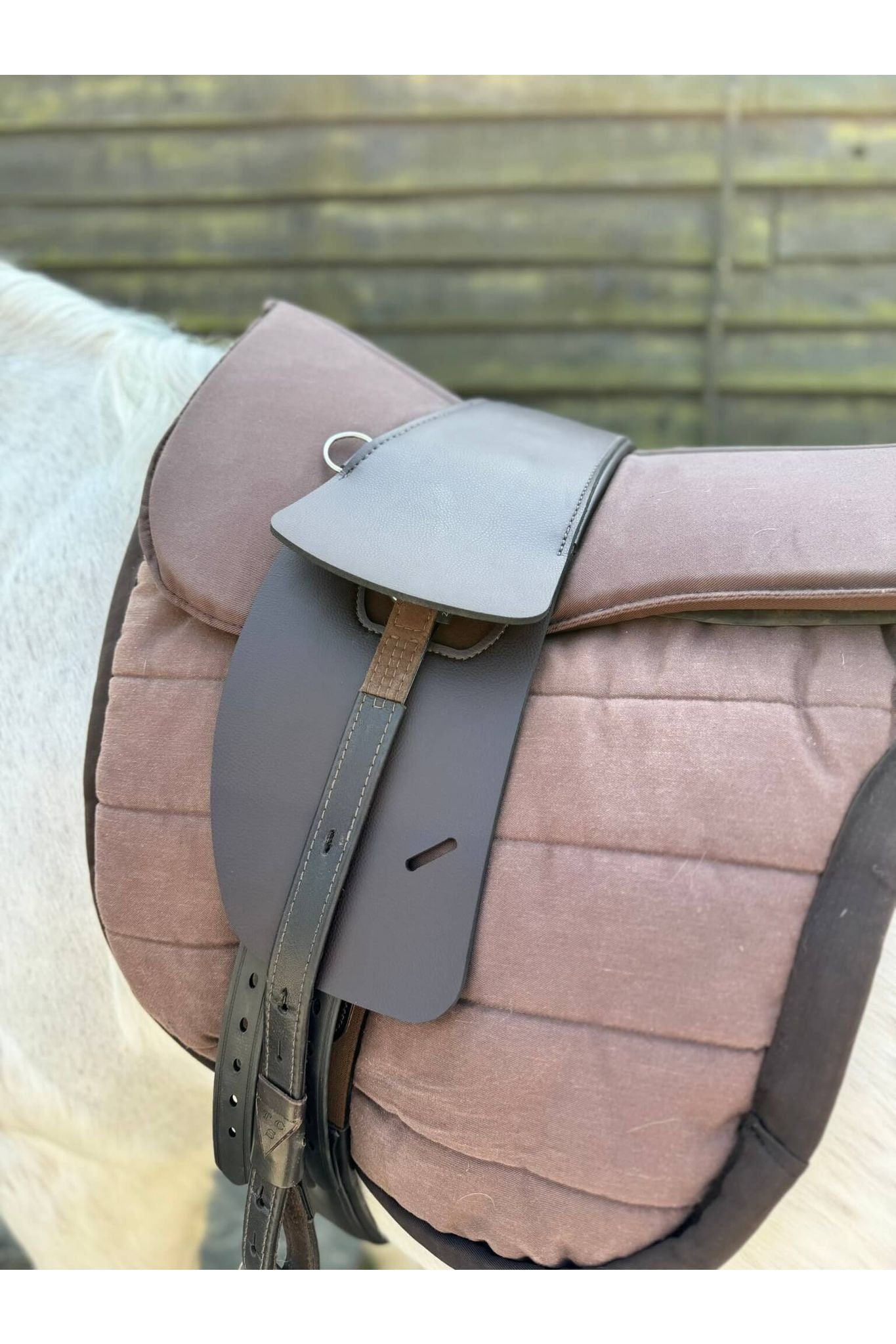 A synthetic chocolate brown treeless Total Contact Saddle on a brown saddle pad and a brown half pad on a grey pony