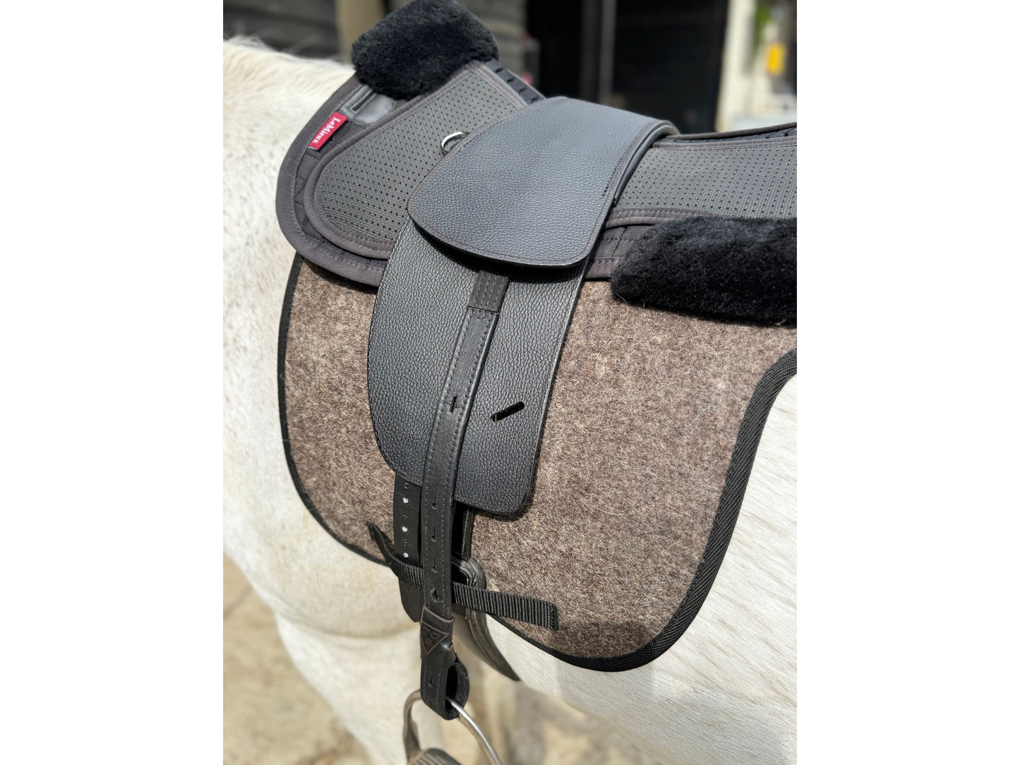 A Classic jet black short billet TCS saddle with black TCS webbers on a grey horse wearing a felt saddle pad and a black half pad