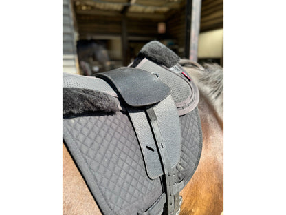 A close up of the Premium black leather TCS saddle with black TCS Webbers on a dark bay horse on a black saddle pad and a black half pad