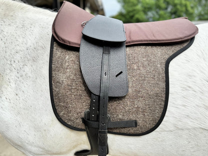A Premium black short billet TCS saddle with black TCS webbers on a grey horse wearing a felt saddle pad and a brown half pad