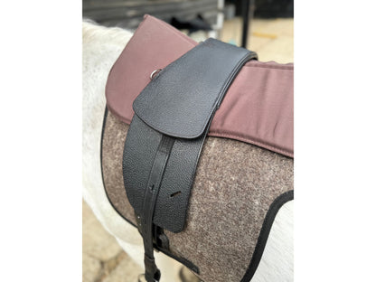 A Premium black short billet TCS saddle with black TCS webbers on a grey horse wearing a felt saddle pad and a brown half pad