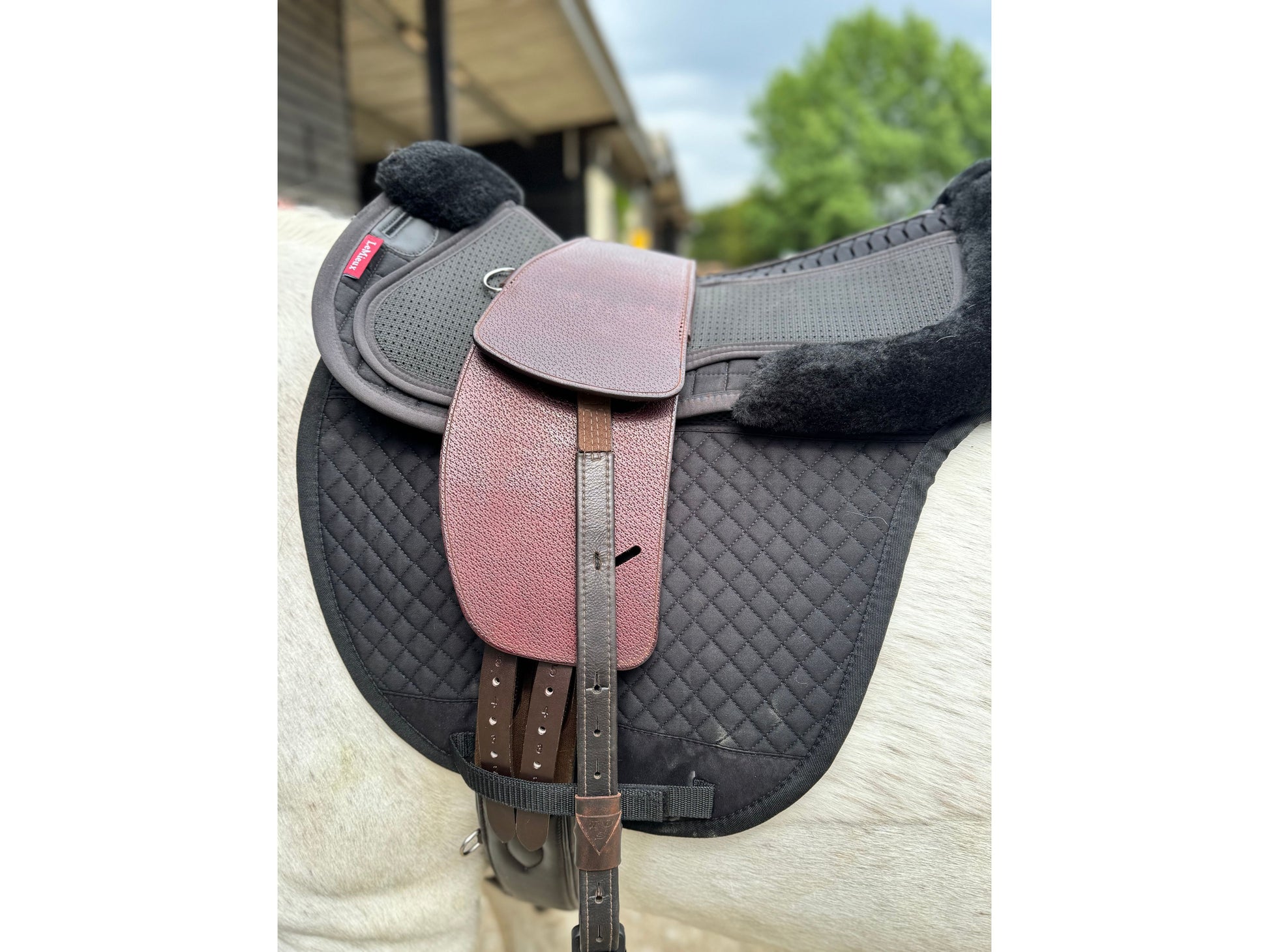 A Premium nutmeg TCS saddle with bown TCS Webbers on a grey horse wearing a black saddle pad and black half pad