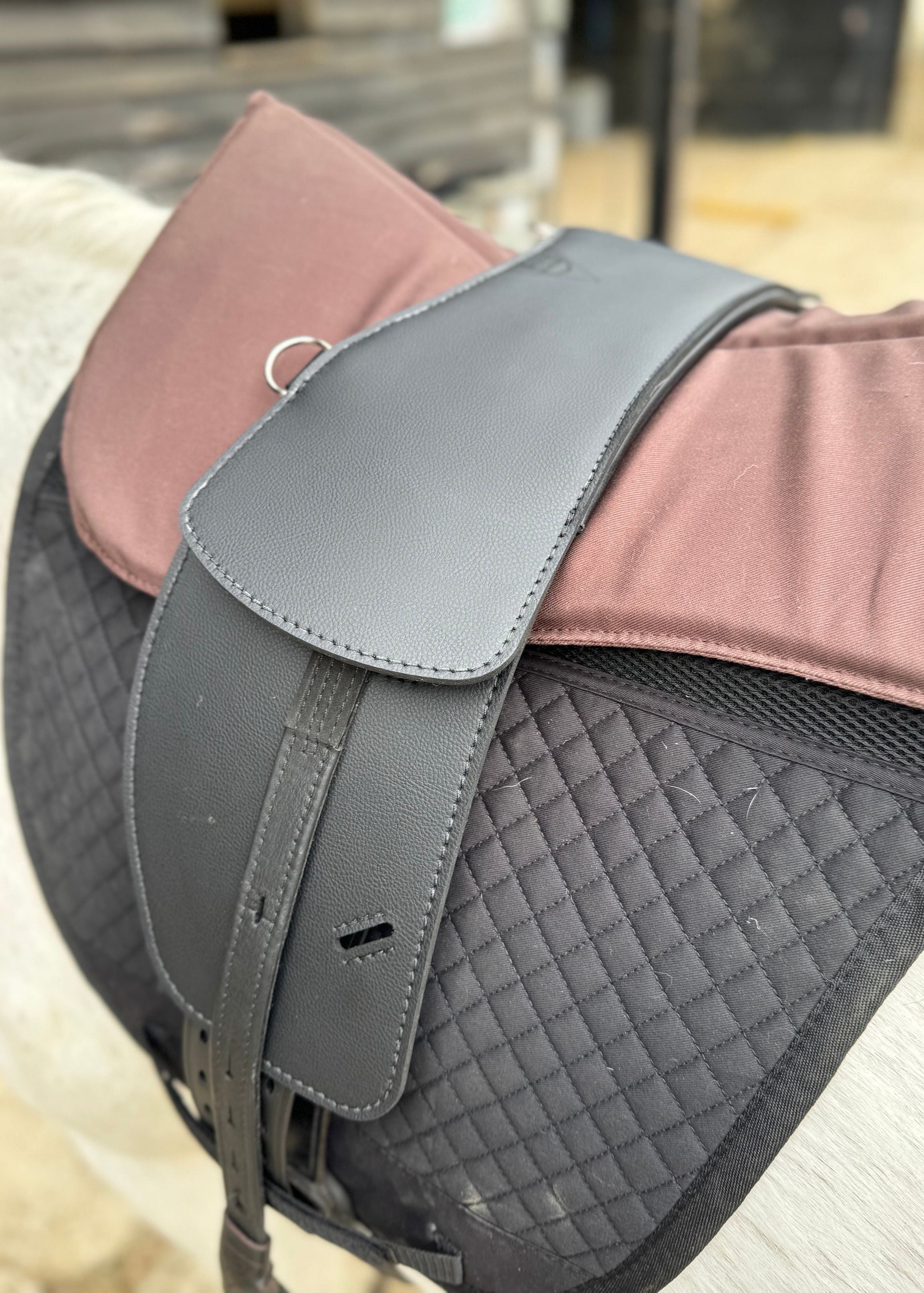 A synthetic black TCS saddle with black TCS Webbers on a grey horse with a black saddle pad and a brown half pad.