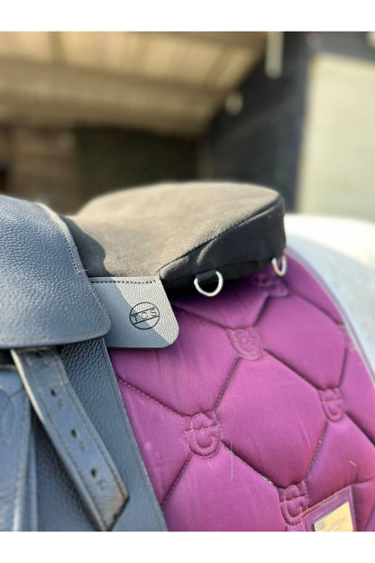A black classic total contact treeless saddle and a black equi-suede saddle seat pad on a grey horse wearing a pink saddle pad