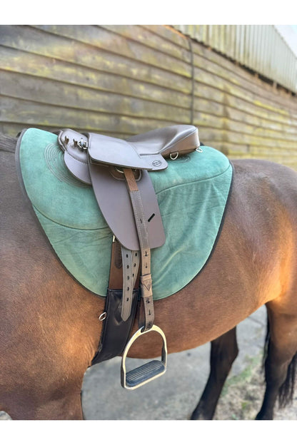 A brown synthetic treeless total contact saddle and a brown synthetic saddle seat pad on a dark bay horse wearing a green saddle pad