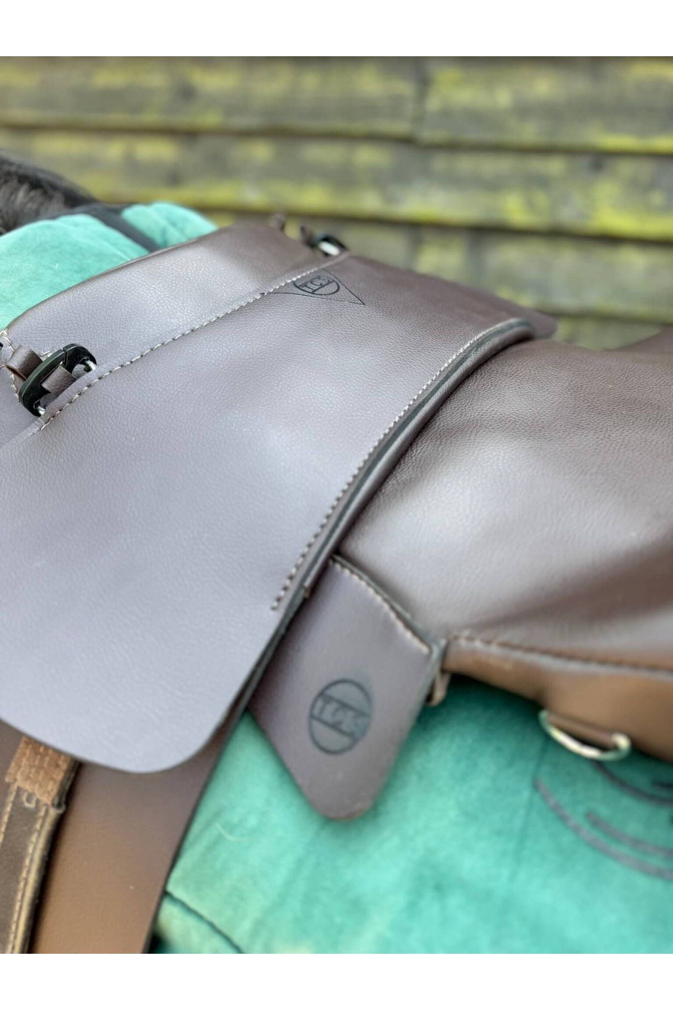 A brown synthetic treeless total contact saddle and a brown synthetic saddle seat pad on a dark bay horse wearing a green saddle pad