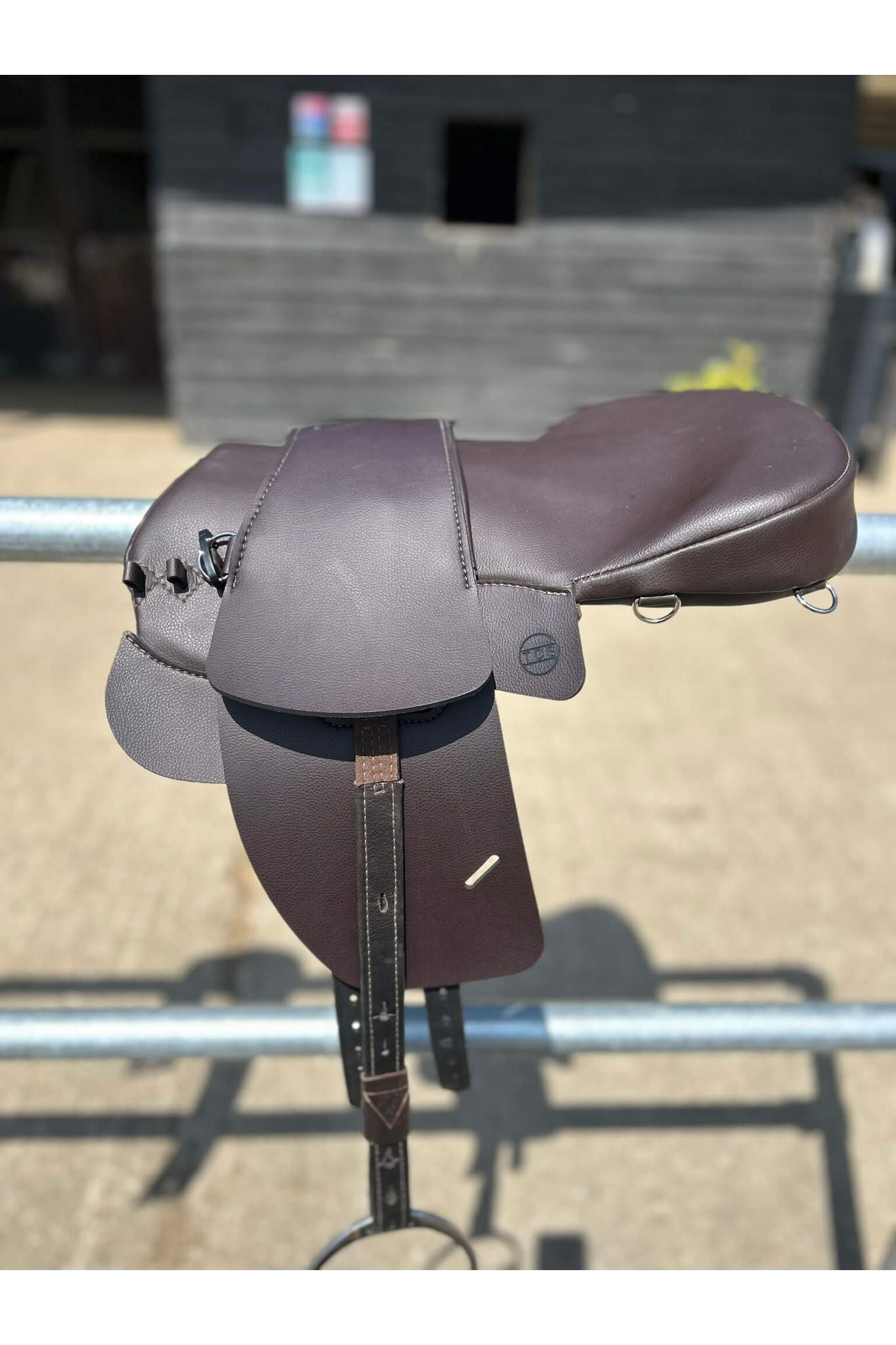 A brown synthetic treeless total contact saddle and a brown synthetic saddle seat pad on a metal railing