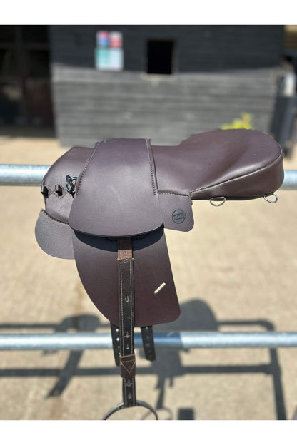 A brown synthetic treeless total contact saddle and a brown synthetic saddle seat pad on a metal railing