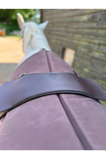 A synthetic chocolate brown treeless Total Contact Saddle close up on a brown saddle pad and a brown half pad on a grey pony