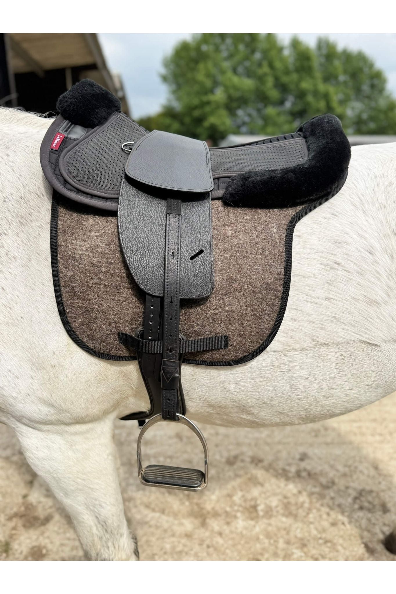A classic black short billet treeless Total Contact Saddle  with TCS Webbers stirrup leathers on a felt saddle pad and a black half pad on a grey pony