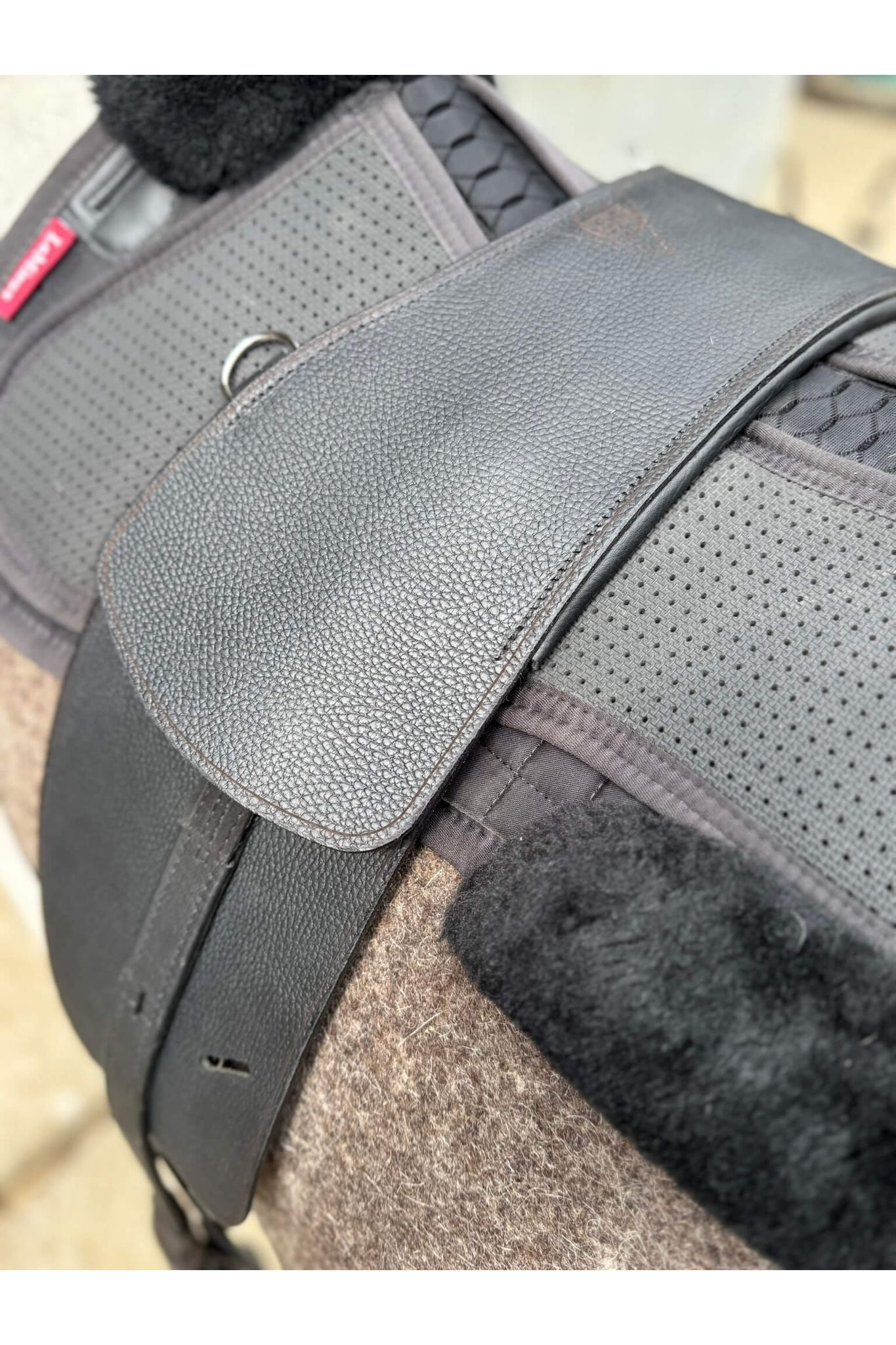 A close up picture of a classic black short billet treeless Total Contact Saddle on a felt saddle pad and a black half pad on a grey pony