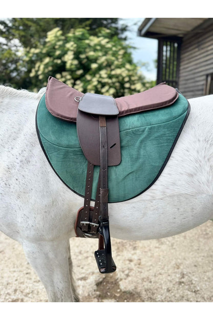 A classic havana brown long billet treeless Total Contact Saddle on a green saddle pad and a brown half pad on a grey pony