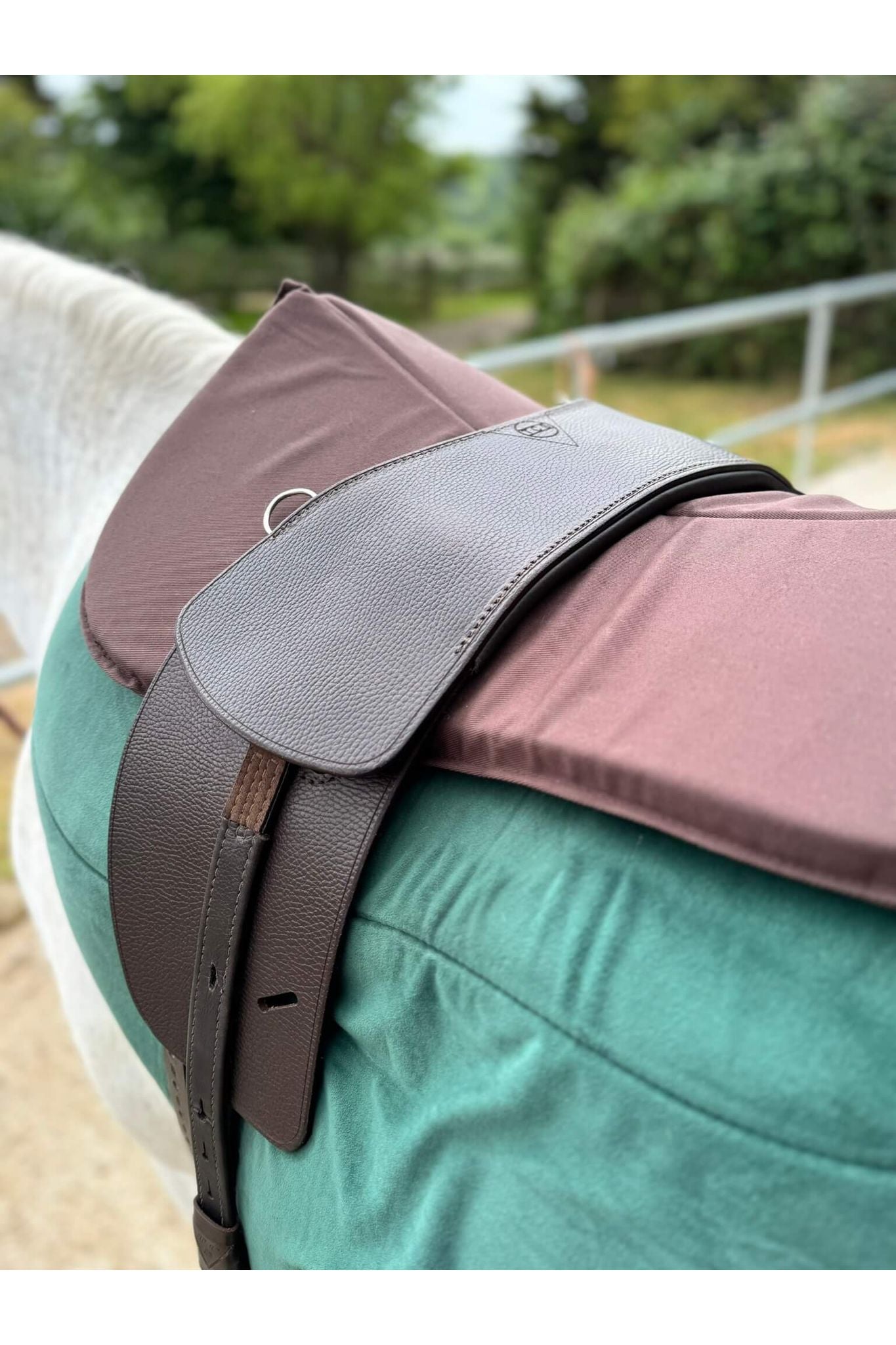 A close-up  of a classic havana brown long billet treeless Total Contact Saddle on a green saddle pad and a brown half pad on a grey pony