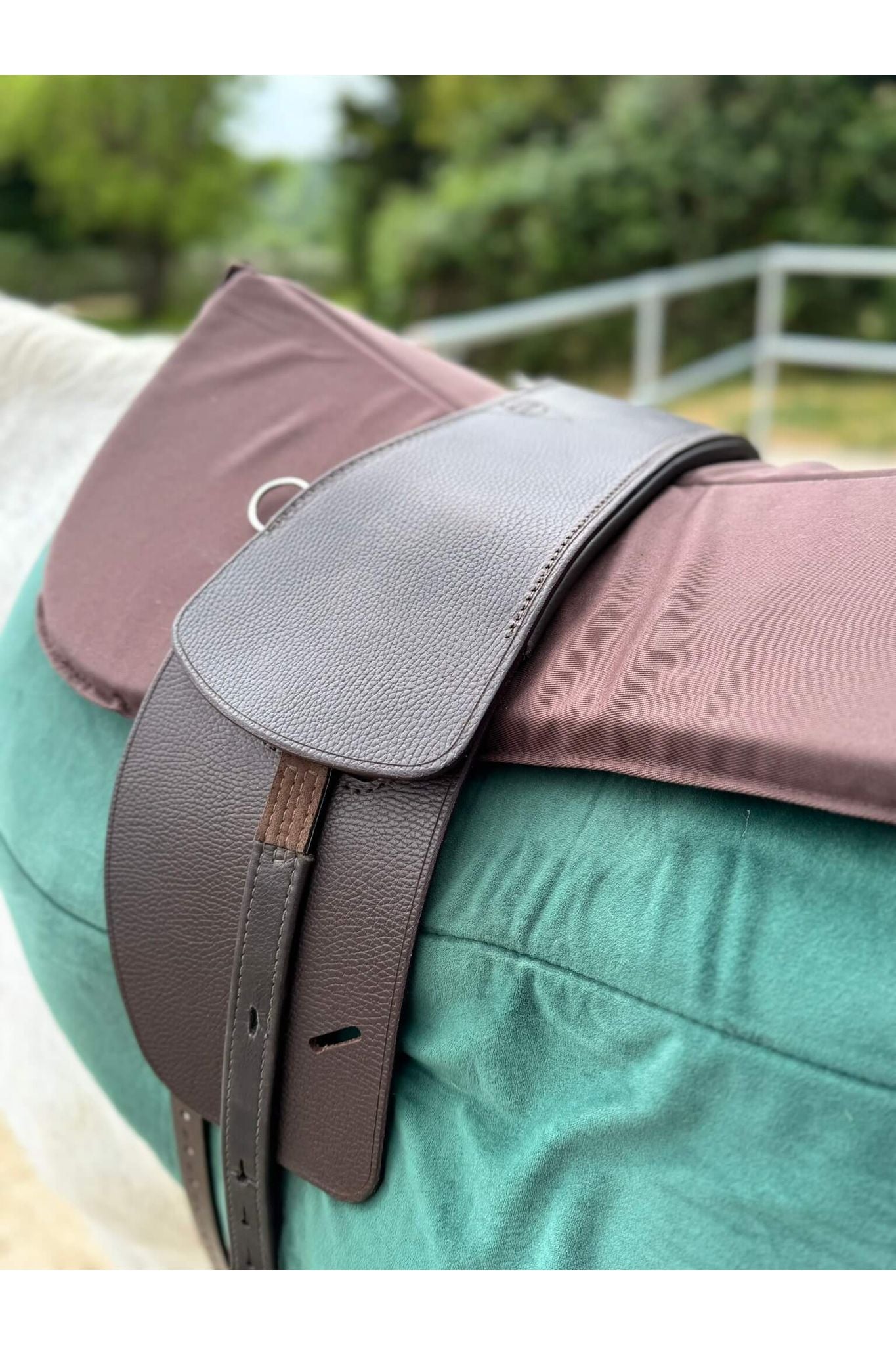 A closeup picture of a classic havana brown long billet treeless Total Contact Saddle on a green saddle pad and a brown half pad on a grey pony