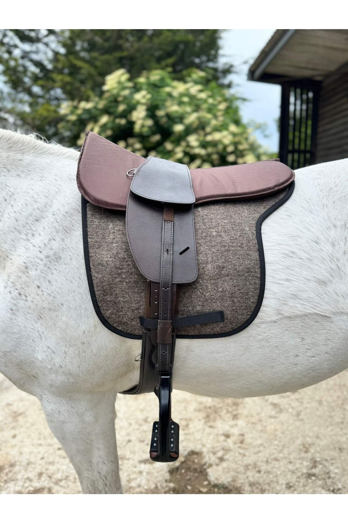 A classic havana brown treeless Total Contact Saddle on a felt saddle pad and a brown half pad on a grey pony