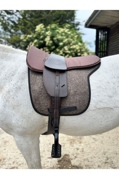 A classic havana brown treeless Total Contact Saddle on a felt saddle pad and a brown half pad on a grey pony