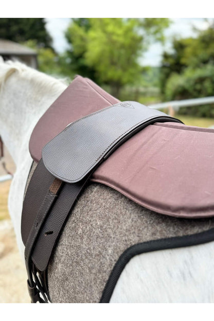 A classic havana brown treeless Total Contact Saddle on a felt saddle pad and a brown half pad on a grey pony