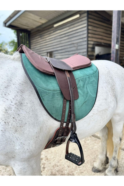 A classic havana brown long billet treeless Total Contact Saddle on a green saddle pad and a brown half pad on a grey pony