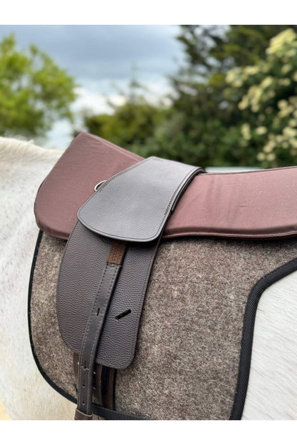 A classic havana brown treeless Total Contact Saddle on a felt saddle pad and a brown half pad on a grey pony