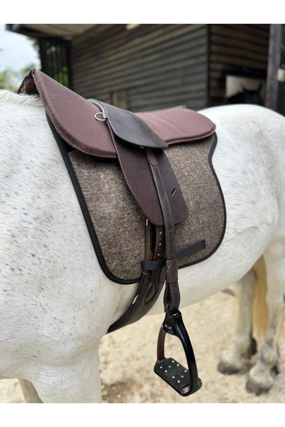 A classic havana brown treeless Total Contact Saddle on a felt saddle pad and a brown half pad on a grey pony