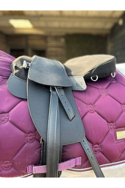A black classic total contact treeless saddle and a black equi-suede saddle seat pad on a grey horse wearing a pink saddle pad