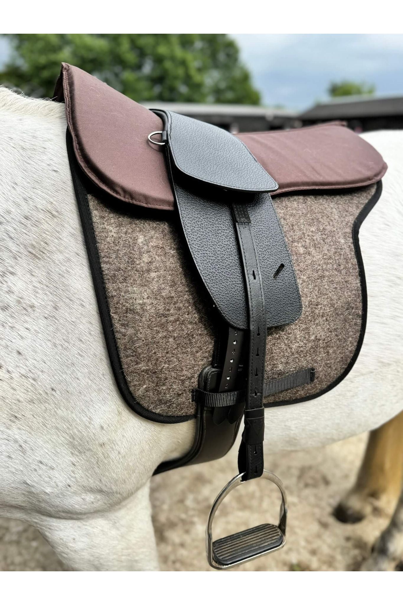 A premium black total contact treeless saddle on a grey horse wearing a felt saddle pad and a brown half pad