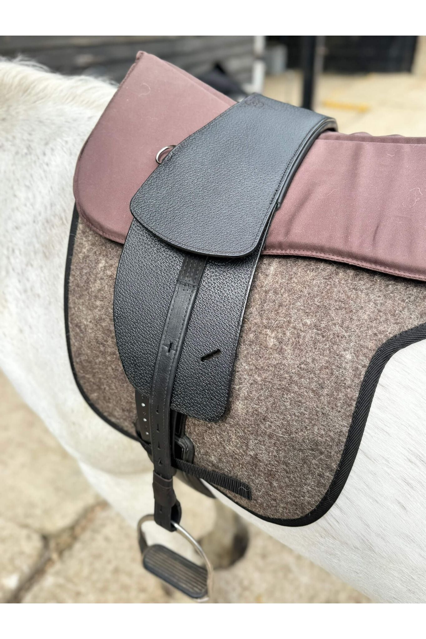 A premium black total contact treeless saddle on a grey horse wearing a felt saddle pad and a brown half pad