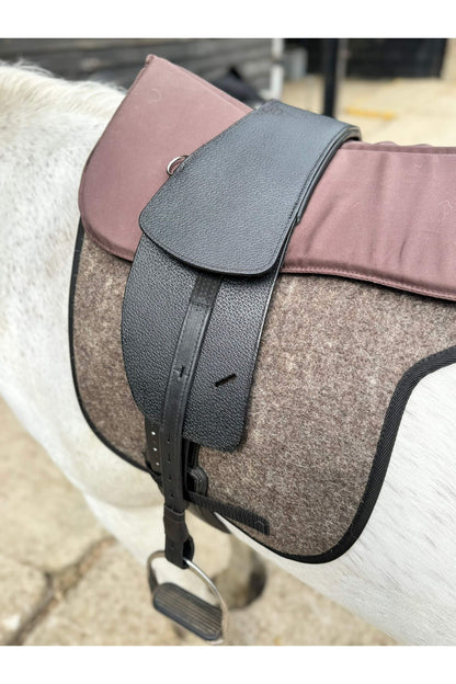 A premium black total contact treeless saddle on a grey horse wearing a felt saddle pad and a brown half pad
