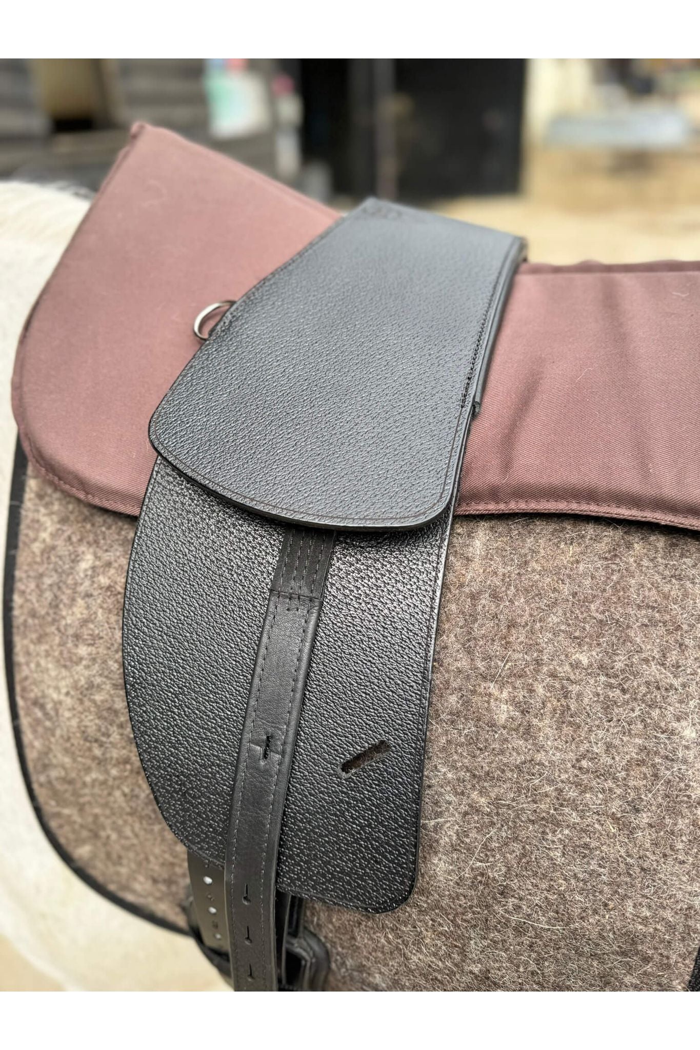 A premium black total contact treeless saddle on a grey horse wearing a felt saddle pad and a brown half pad