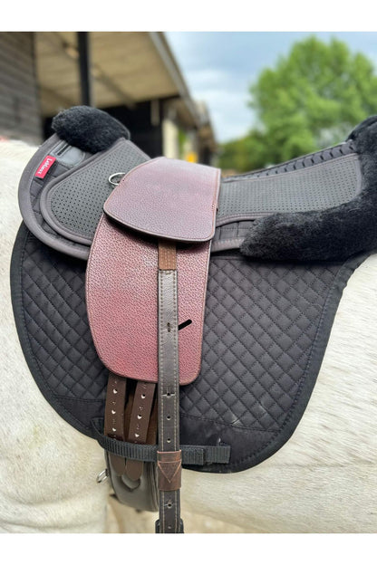 A premium nutmeg total contact treeless saddle on a grey horse wearing a black saddle pad and a black half pad