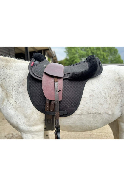 A premium nutmeg total contact treeless saddle on a grey horse wearing a black saddle pad and a black half pad