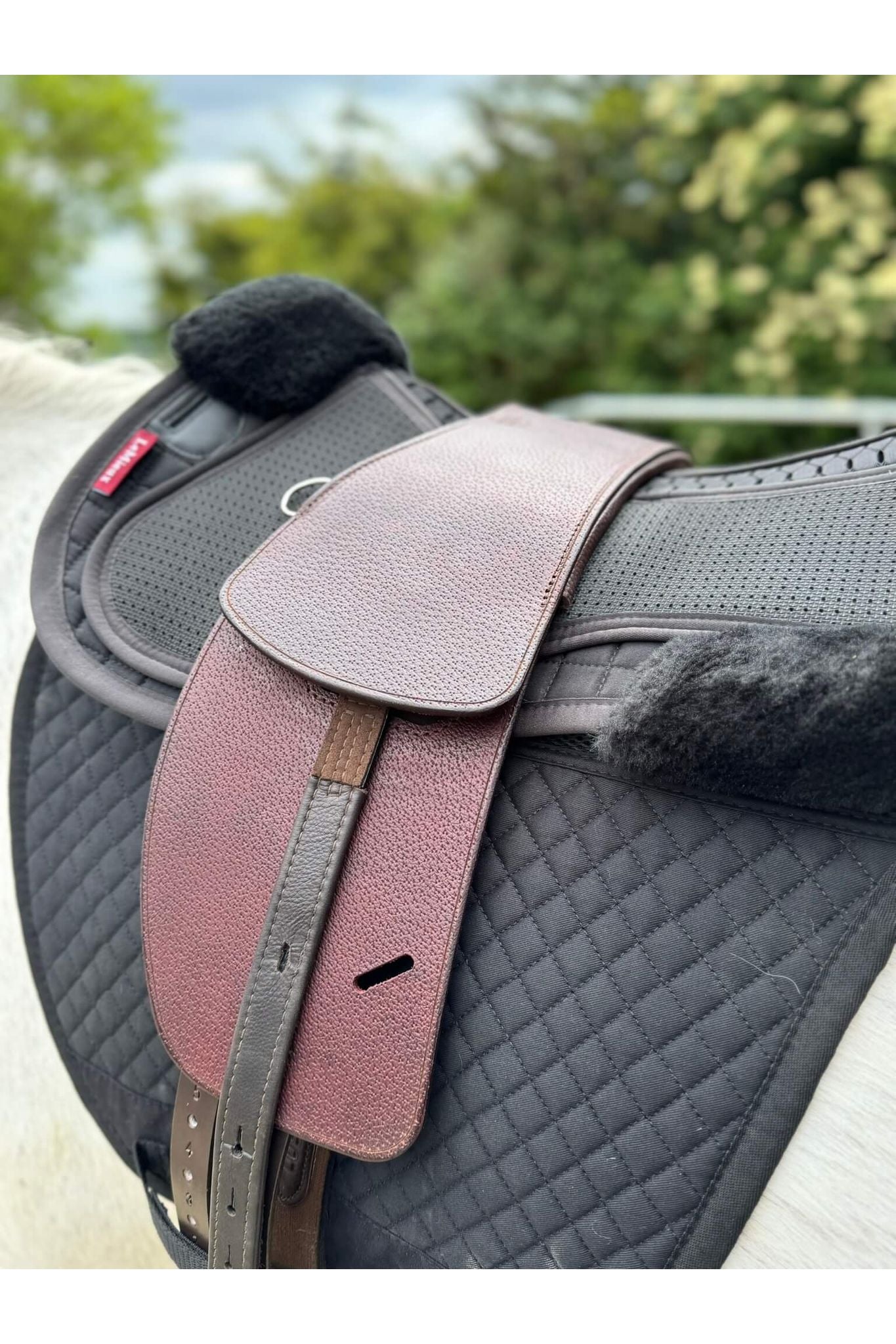 A premium nutmeg total contact treeless saddle on a grey horse wearing a black saddle pad and a black half pad
