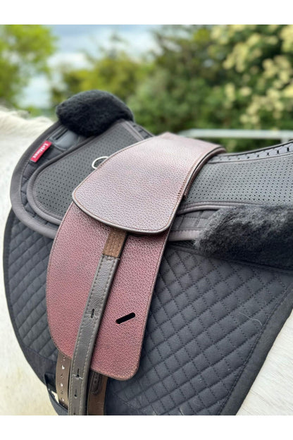 A premium nutmeg total contact treeless saddle on a grey horse wearing a black saddle pad and a black half pad