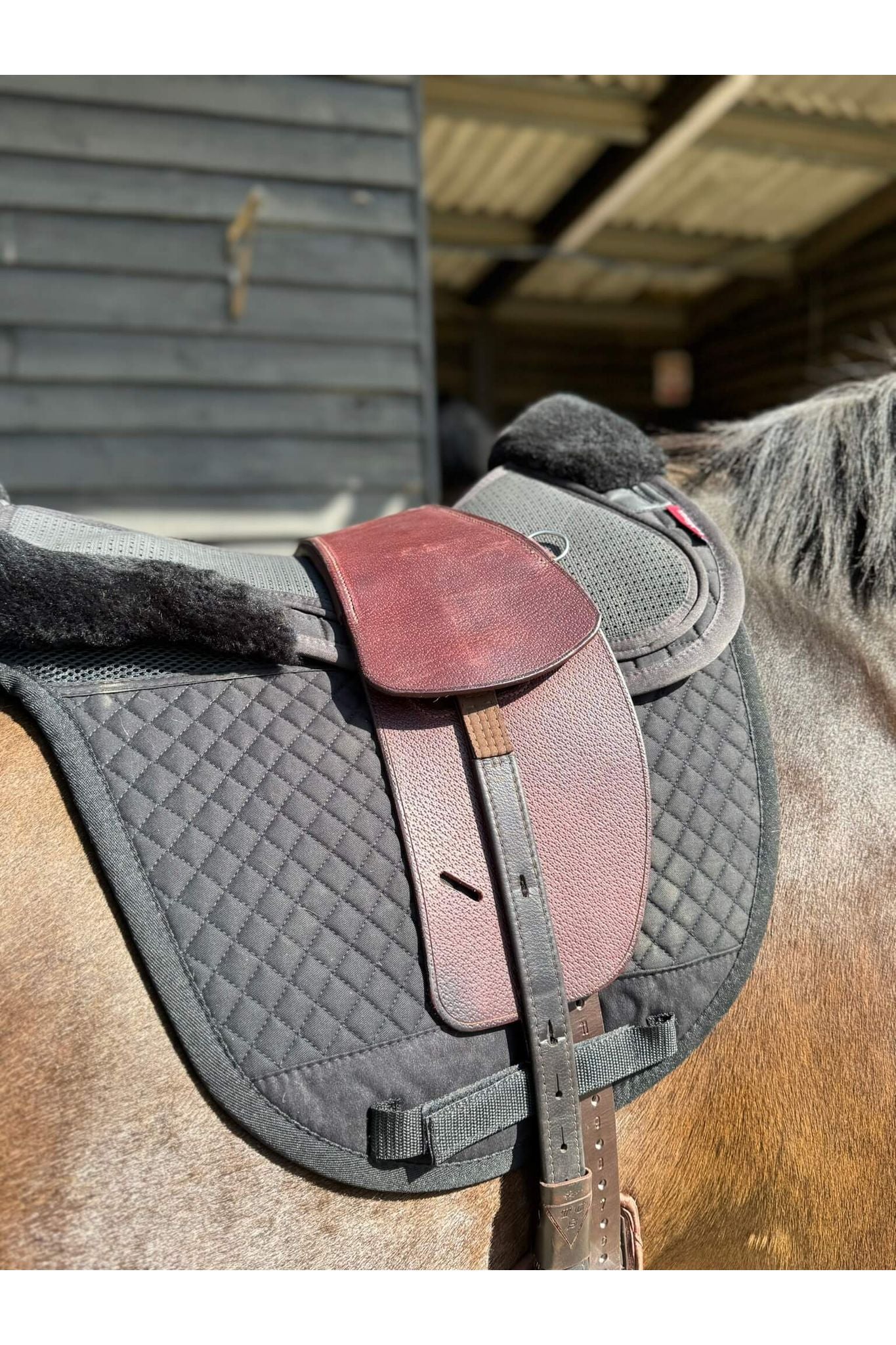 A premium nutmeg total contact treeless saddle on a dark bay horse wearing a black saddle pad and a black half pad