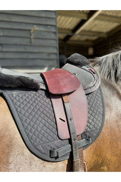 A premium nutmeg total contact treeless saddle on a dark bay horse wearing a black saddle pad and a black half pad