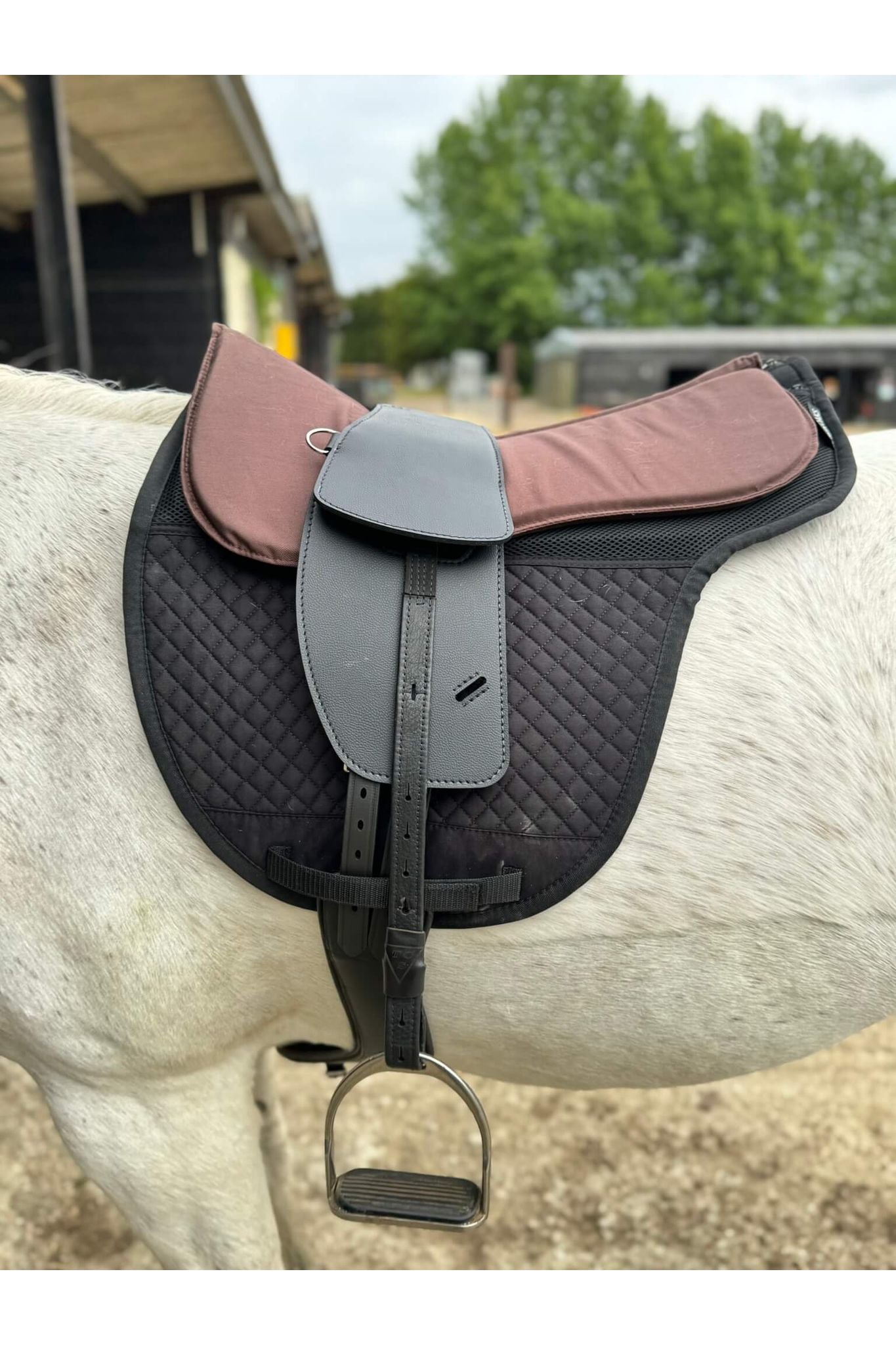 A synthetic black short billet Total Contact Saddle close up on a black saddle pad and a brown half pad on a grey pony