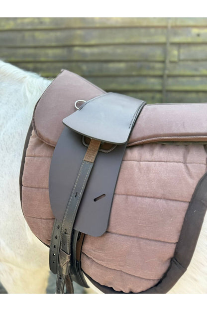 A synthetic chocolate brown treeless Total Contact Saddle on a brown saddle pad and a brown half pad on a grey pony