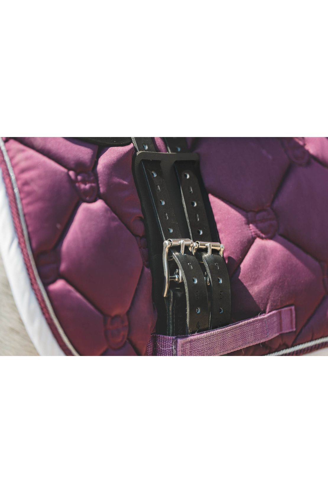 A girth guard being used to protect a horse from the girth buckles is being used on top of a pink saddle pad