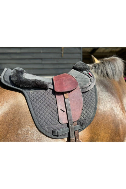 A premium nutmeg total contact treeless saddle on a dark bay horse wearing a black saddle pad and a black half pad